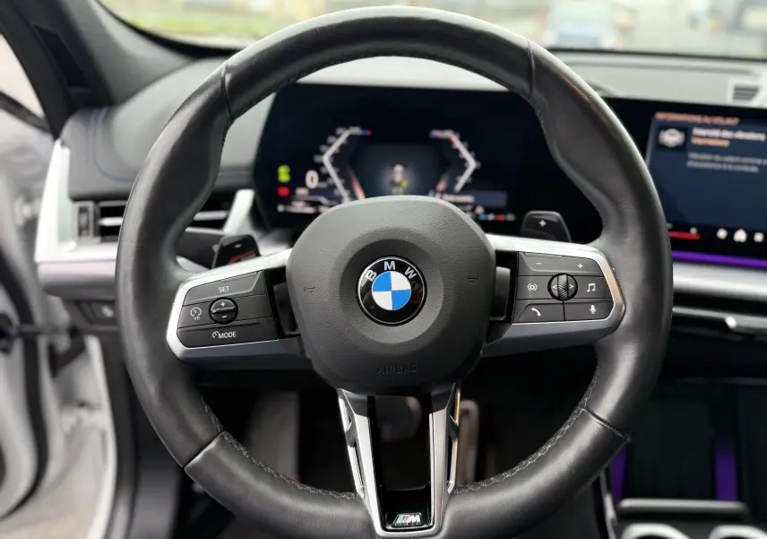 Vue rapprochée du volant en cuir noir M Sport d'une BMW X1 18D 2025 avec tableau de bord numérique en arrière-plan.