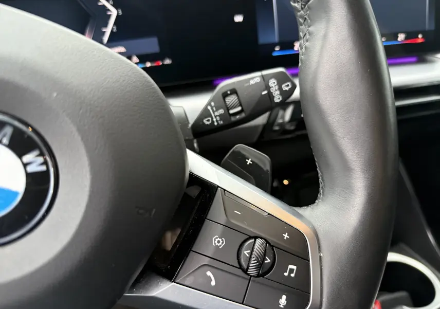 Gros plan sur le volant cuir noir de la BMW X1 18D 2025, montrant les commandes multifonctions côté droit.