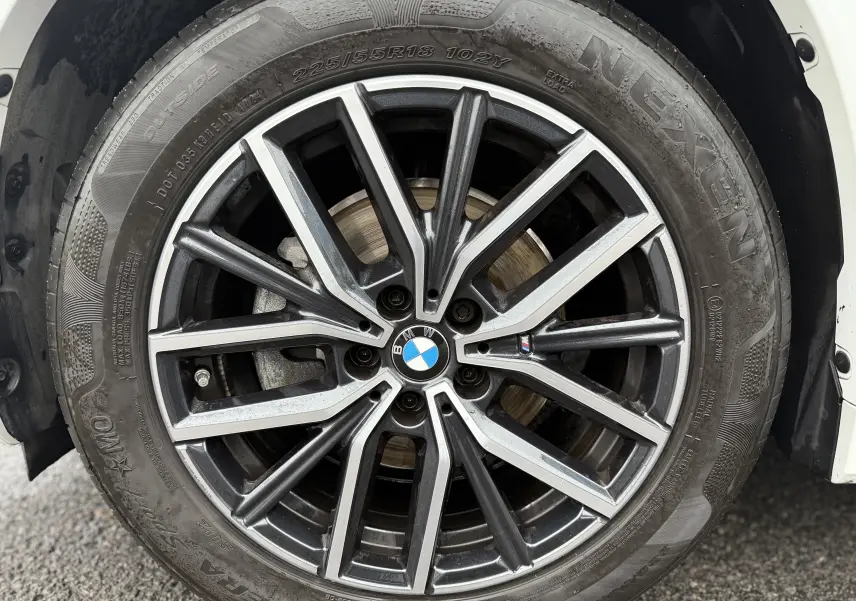 Gros plan sur la jante alliage noire et argentée d'un BMW X1 blanc minéral 2025, mettant en valeur le logo BMW central.