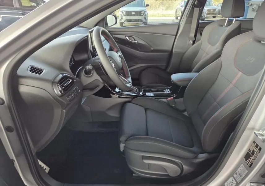 Vue intérieure côté conducteur de la Hyundai i30 SW N-LINE 2025 avec sièges tissu noirs et surpiqûres rouges.