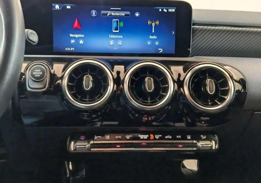 Vue rapprochée du tableau de bord noir brillant du Mercedes GLA 250 e 2023 avec écran tactile et trois aérateurs ronds chromés.