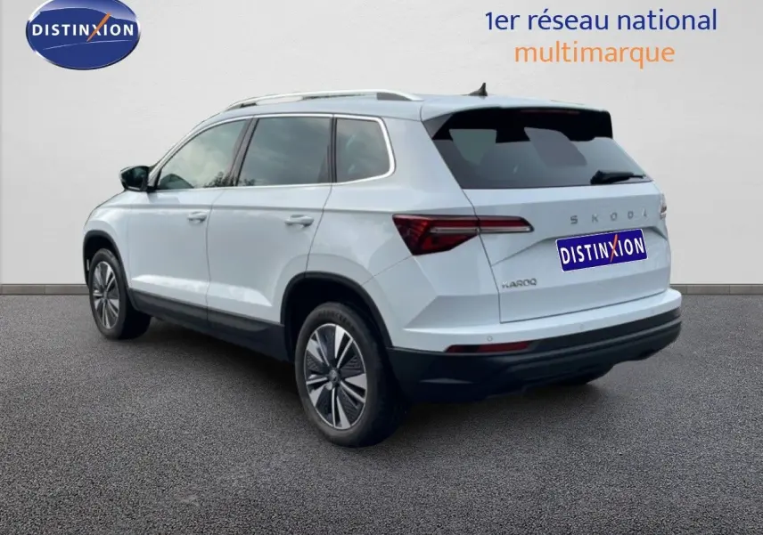 Vue 3/4 arrière droite d’un Skoda Karoq blanc glacier avec jantes bi-ton et vitres teintées.