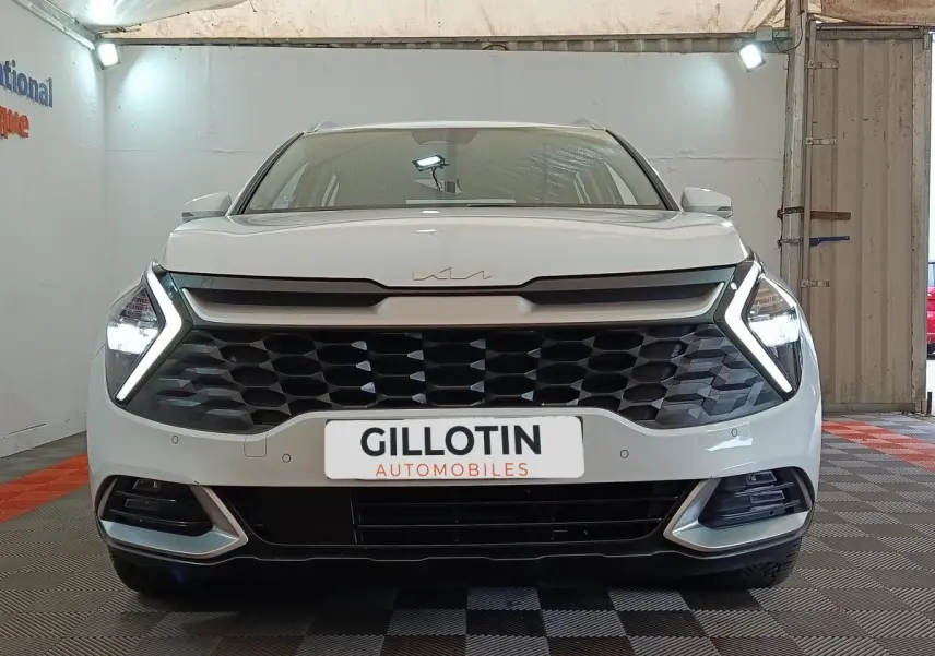 Vue frontale d’un KIA Sportage blanc 2022 avec calandre noire et feux LED en forme de flèche allumés.