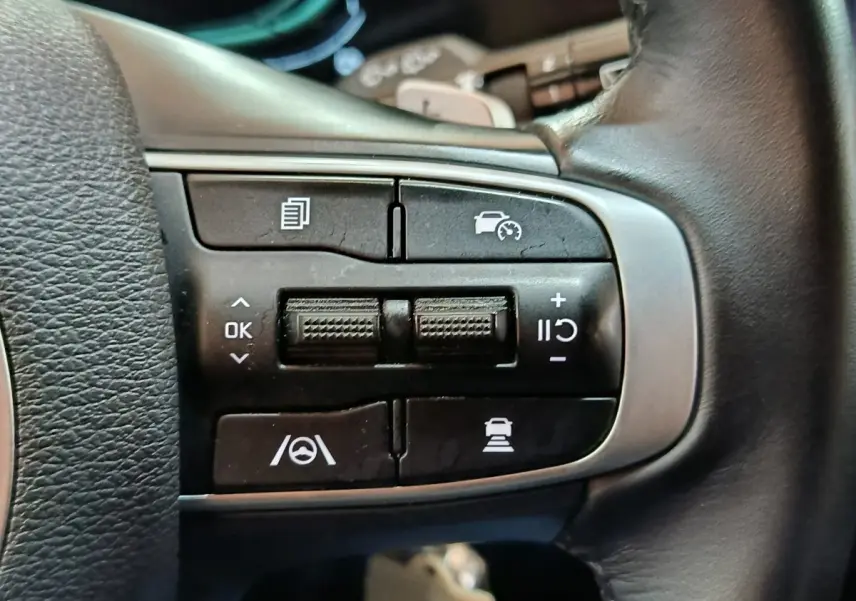 Gros plan sur les commandes du volant en cuir du Kia Sportage blanc, version hybride rechargeable 2022.