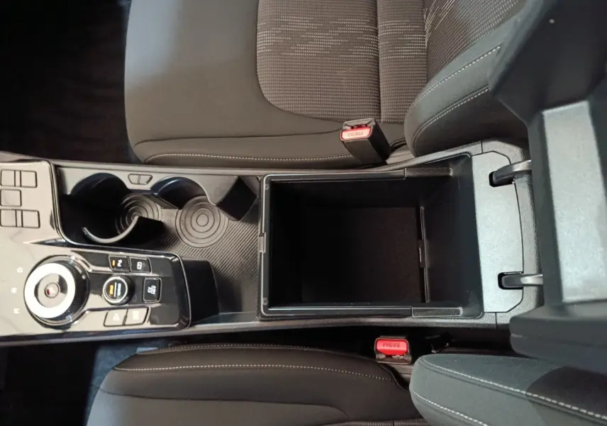 Vue plongeante sur la console centrale noire du Kia Sportage blanc 2022, avec rangement ouvert et commandes de boîte auto.