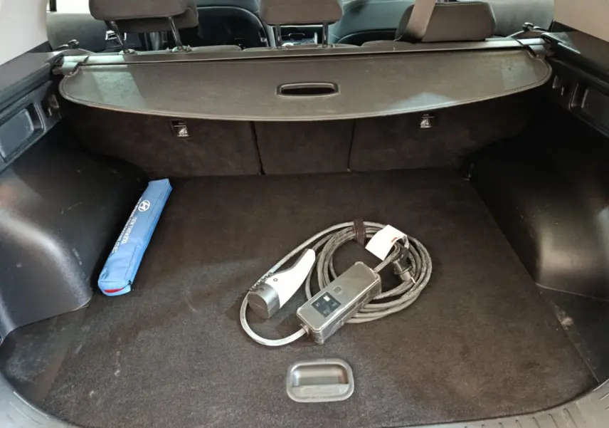 Coffre ouvert d’un KIA Sportage blanc 2022, vue intérieure montrant câble de recharge et rangement noir.