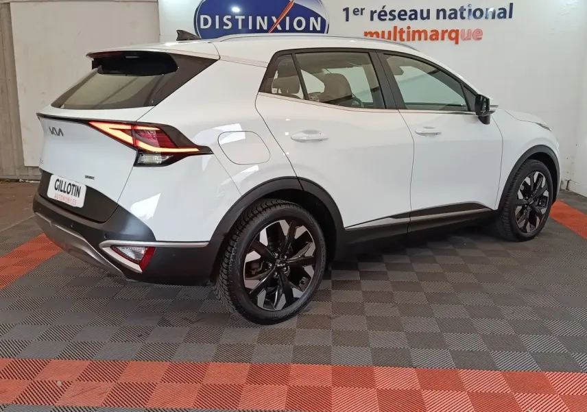 Vue 3/4 arrière droite d'un KIA Sportage blanc 2022 avec jantes noires et feux arrière LED allumés.
