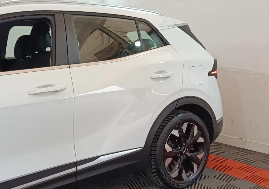 Vue côté droit arrière du Kia Sportage blanc 2022 avec jantes noires et feux arrière LED allumés.