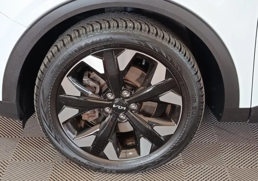 Gros plan sur la roue avant droite du Kia Sportage blanc 2022 avec jante alliage noire et argentée design moderne.