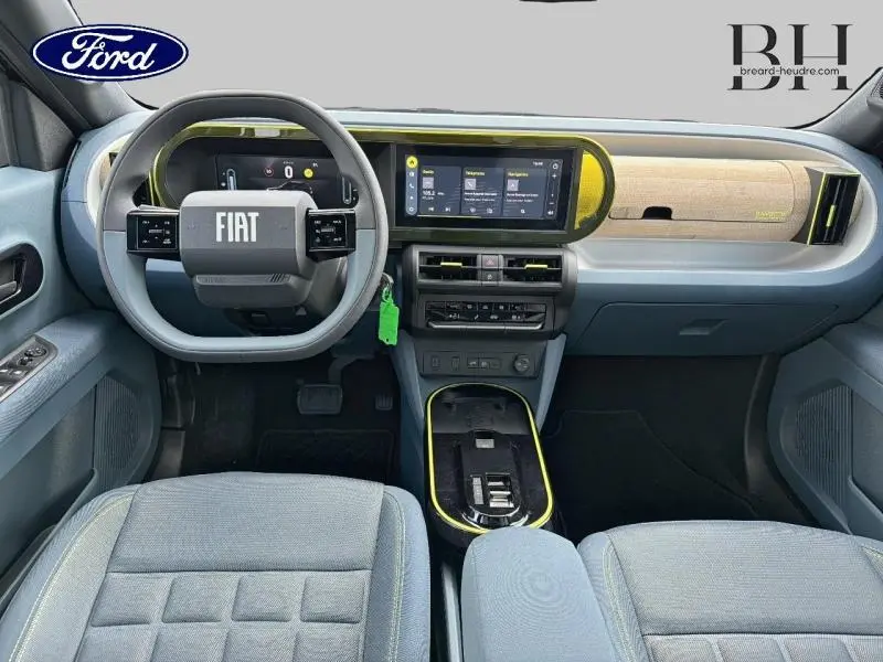 Vue intérieure avant de la Fiat Grande Panda 2025, tableau de bord bleu clair avec écran tactile et volant multifonction gris.