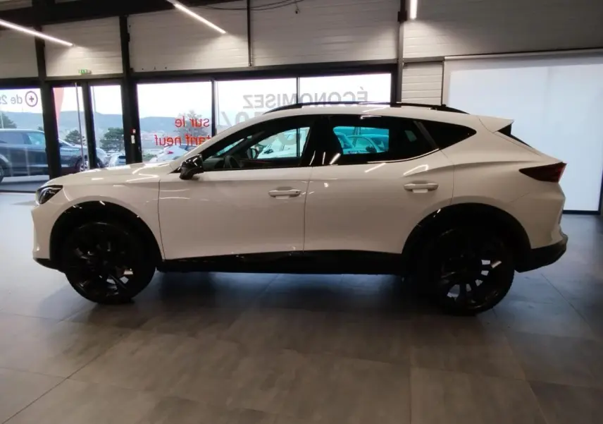 Vue de profil côté gauche d'un CUPRA Formentor blanc Nevada avec jantes noires en intérieur showroom.
