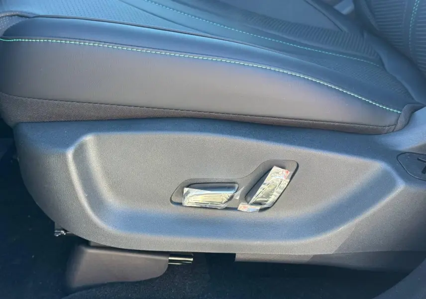 Gros plan sur les commandes électriques du siège conducteur noir avec surpiqûres vertes du BYD SEAL U 2026.