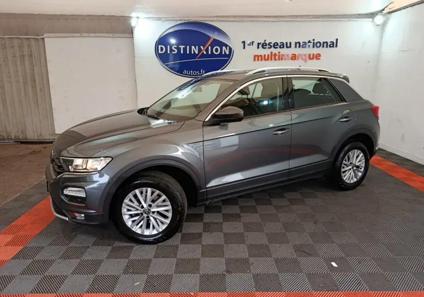 Volkswagen T-Roc gris foncé vu de profil côté gauche dans un showroom avec logo Distinxion en arrière-plan.