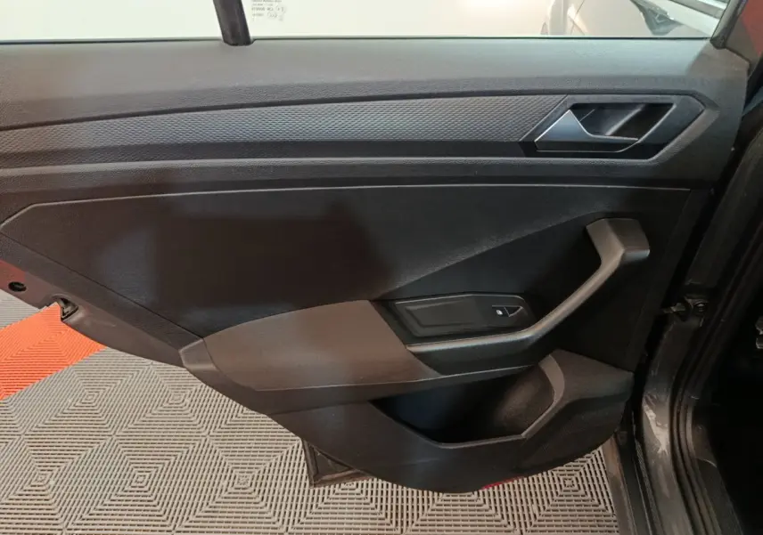 Intérieur côté gauche de la porte d'une Volkswagen T-Roc gris foncé, avec poignée et commande de vitre électrique.
