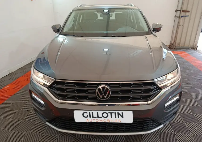 Vue avant d'un Volkswagen T-Roc gris foncé avec calandre hexagonale et phares LED allumés dans un showroom.