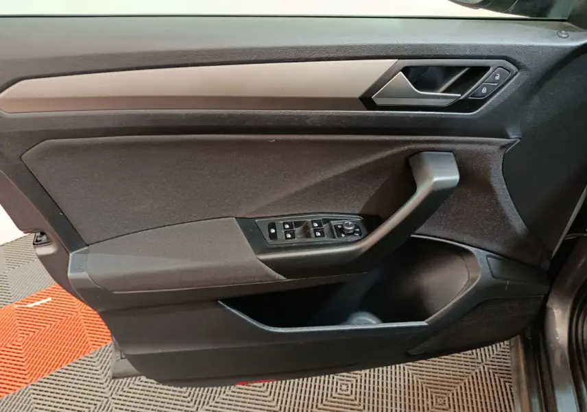 Vue rapprochée de la porte avant gauche du Volkswagen T-Roc gris foncé, montrant les commandes de vitres et la poignée noire.