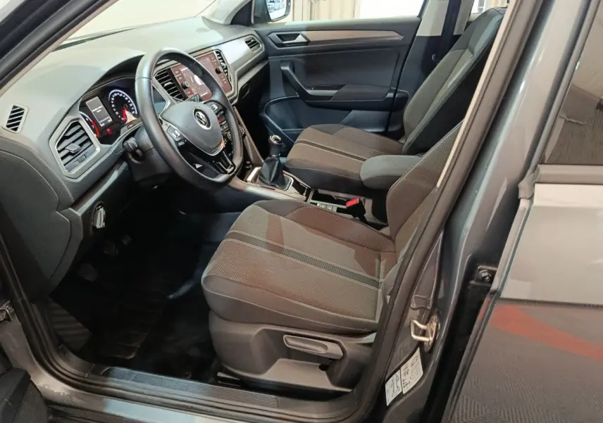 Vue intérieure côté conducteur du Volkswagen T-Roc gris foncé 2021, avec volant cuir et boîte manuelle visible.