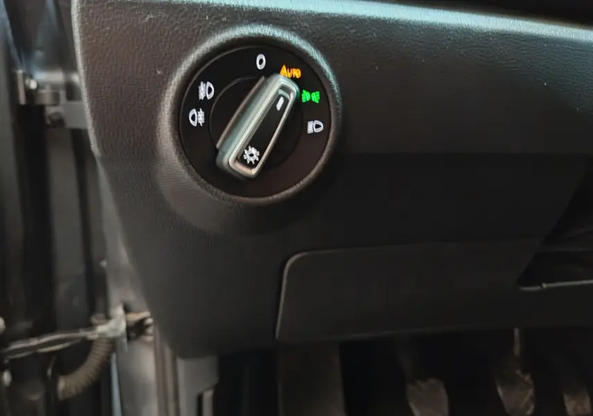 Gros plan sur le bouton de commande des phares à gauche du tableau de bord d'un Volkswagen T-Roc gris foncé.