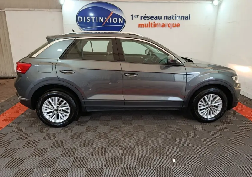 Profil côté droit d'un Volkswagen T-Roc gris foncé 2021 garé en intérieur avec jantes alliage et rails de toit noirs.