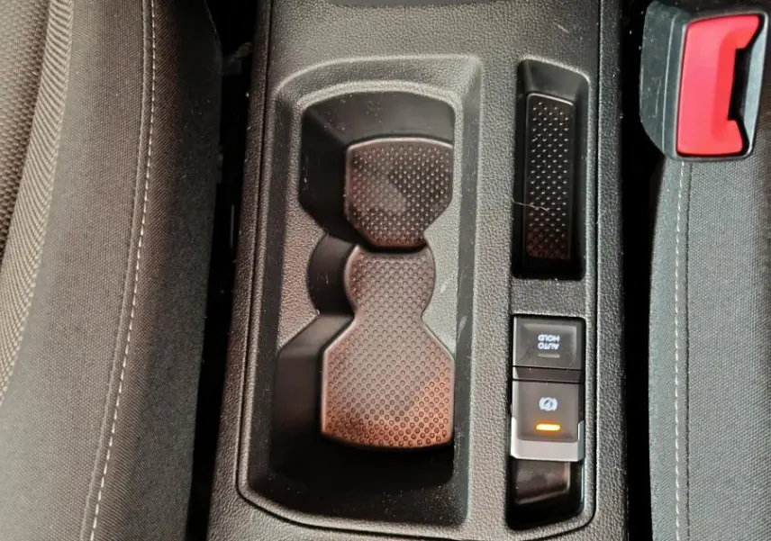 Gros plan sur la console centrale noire du Volkswagen T-Roc 2021, avec porte-gobelets et frein à main électrique.