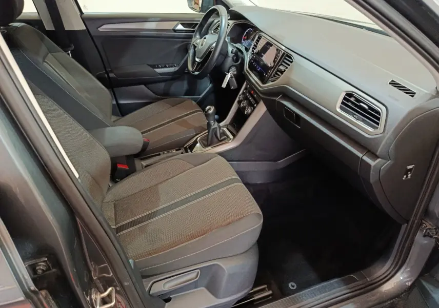 Intérieur avant droit du Volkswagen T-Roc gris foncé 2021, montrant sièges tissu, volant cuir et tableau de bord tactile.