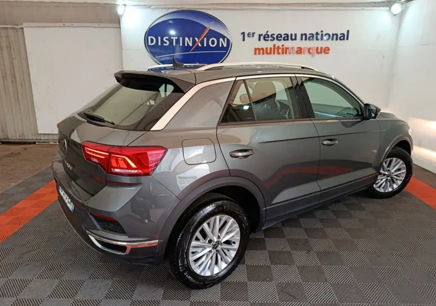 Vue 3/4 arrière droite d'un Volkswagen T-Roc gris foncé avec jantes alliage et barres de toit noires.