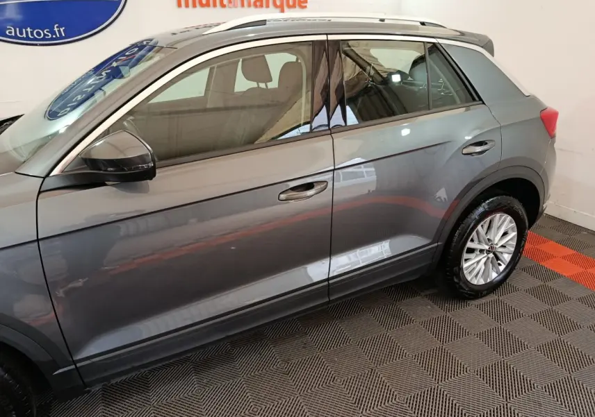 Profil côté gauche du Volkswagen T-Roc gris foncé 2021 avec jantes alliage et barres de toit noires visibles.
