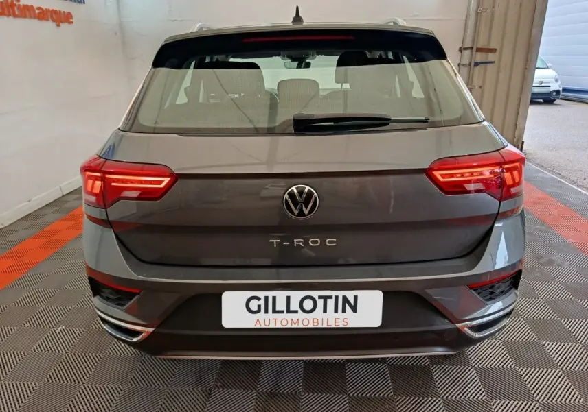 Vue arrière d'un Volkswagen T-Roc gris foncé avec feux LED et logo VW bien visibles dans un garage.