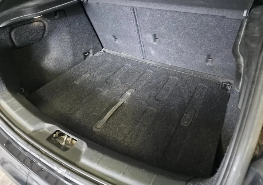 Coffre ouvert vu de dessus d'une Volvo V40 D2 R-Design noire, montrant le tapis de sol et les fixations arrière.