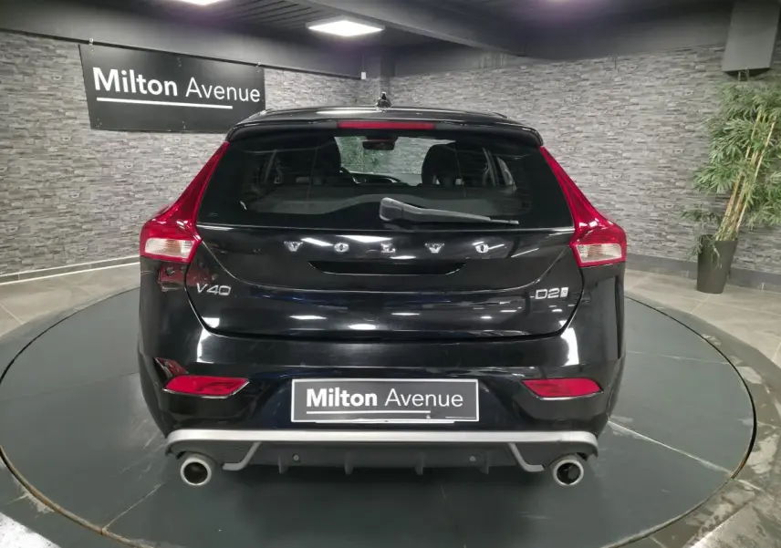 Vue arrière d'une Volvo V40 D2 noire avec double sortie d'échappement et feux arrière LED dans un showroom.