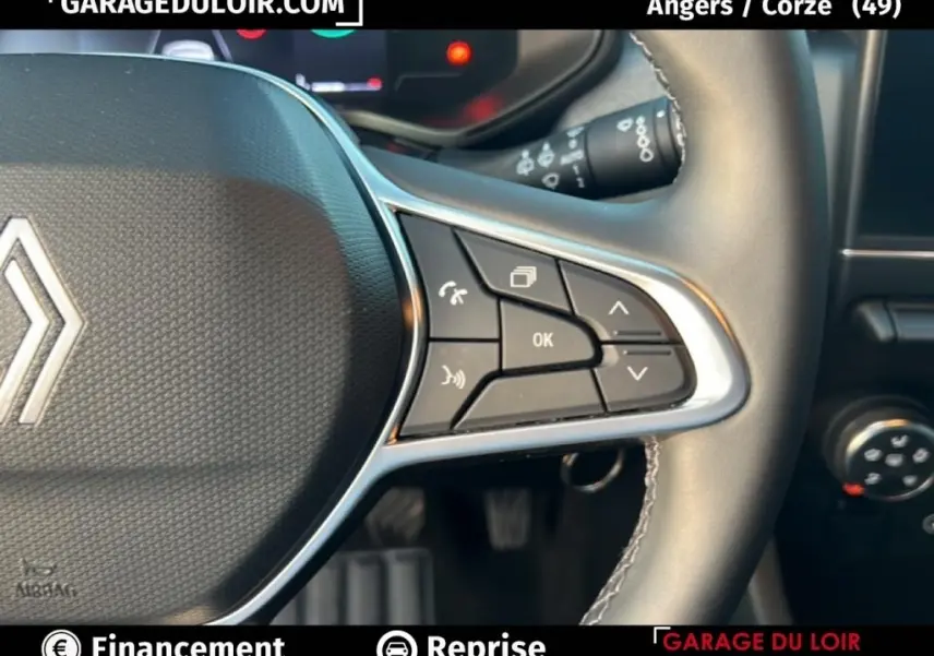 Gros plan sur le volant cuir synthétique noir de la Renault Clio 2025, avec commandes multifonctions et logo central visible.