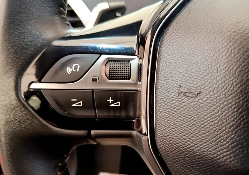 Gros plan sur les commandes gauche du volant en cuir noir du Peugeot 3008 bleu, version Active Pack 2022.