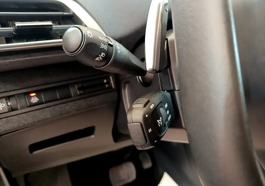 Gros plan sur la commande multifonction noire et le commodo d’éclairage à gauche du volant noir du Peugeot 3008 bleu.
