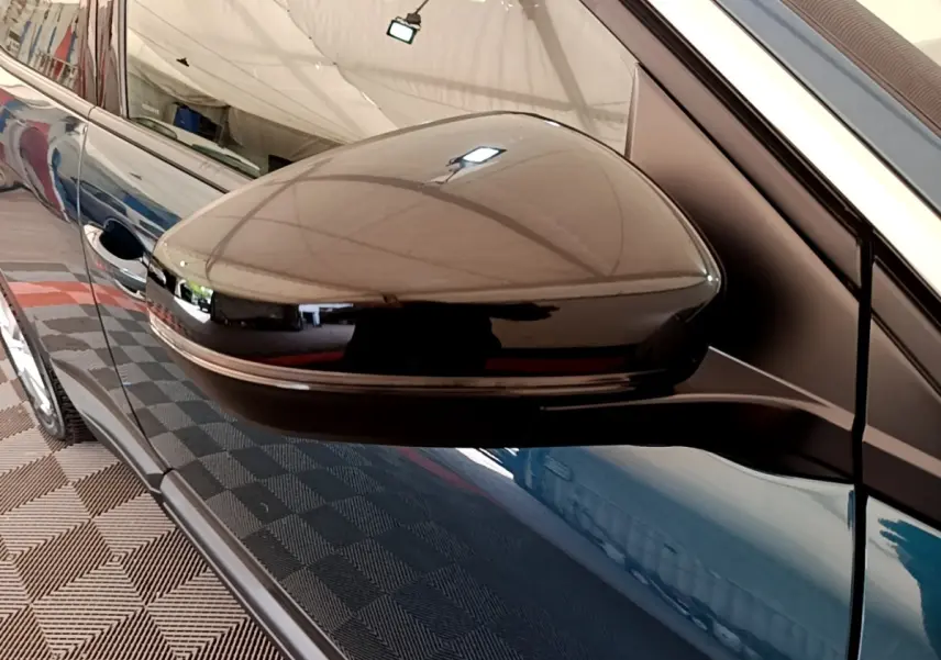 Gros plan sur le rétroviseur noir côté gauche d’un Peugeot 3008 bleu, reflet de l’environnement intérieur visible.