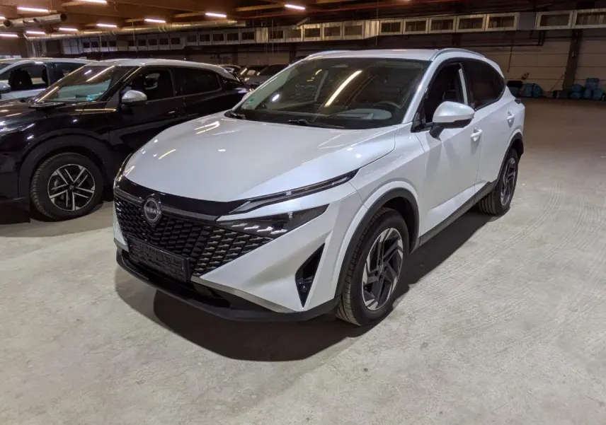 Nissan Qashqai blanc nacré vu en 3/4 avant droit dans un parking intérieur avec calandre noire distinctive.