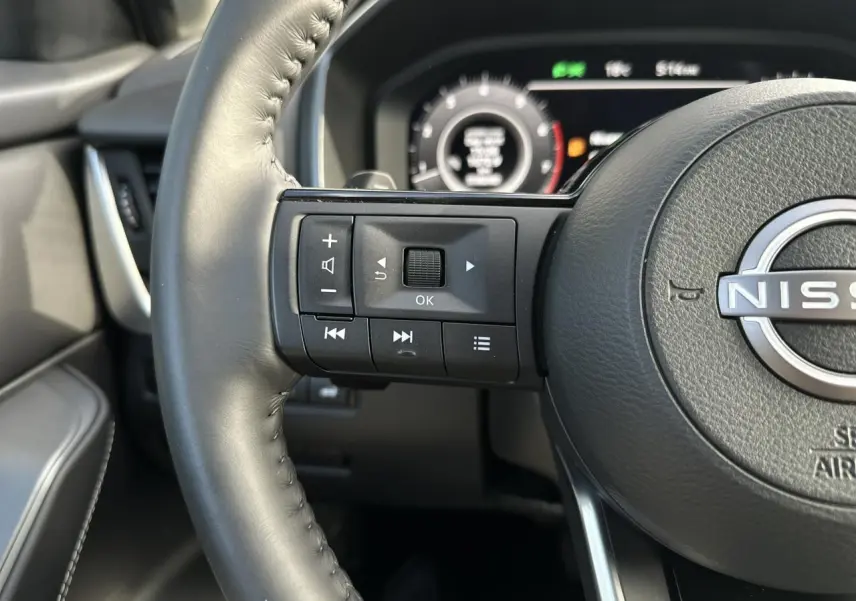 Gros plan sur le volant cuir noir du Nissan Qashqai 2025 avec commandes audio et tableau de bord numérique en arrière-plan.