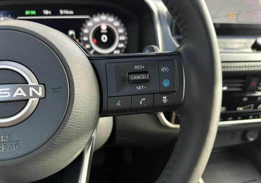 Gros plan sur le volant cuir noir du Nissan Qashqai 2025 avec commandes de régulateur de vitesse et tableau de bord numérique.