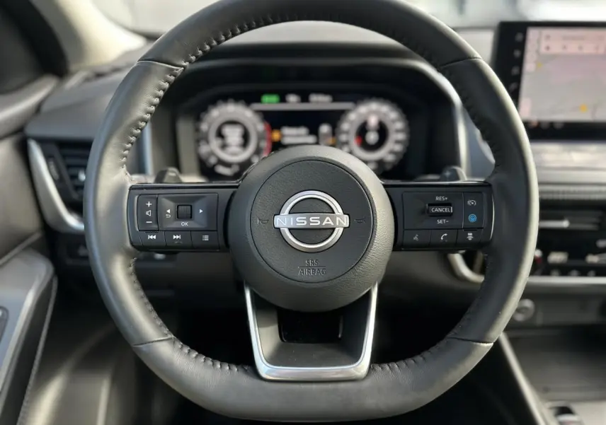 Volant cuir noir de Nissan Qashqai 2025 vu de face, avec commandes intégrées et tableau de bord numérique flou en arrière-plan.