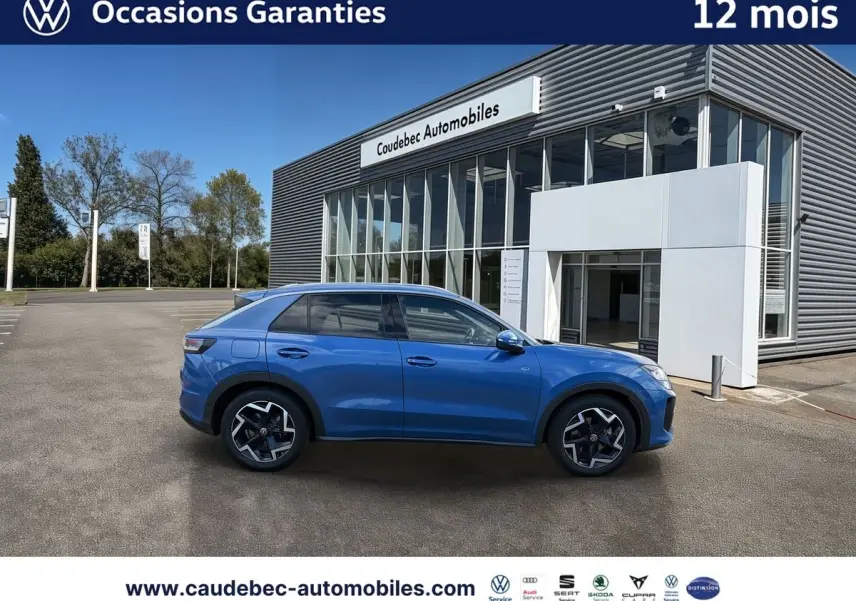Vue de profil côté gauche d'un Volkswagen T-Roc bleu métallisé garé devant un bâtiment moderne.