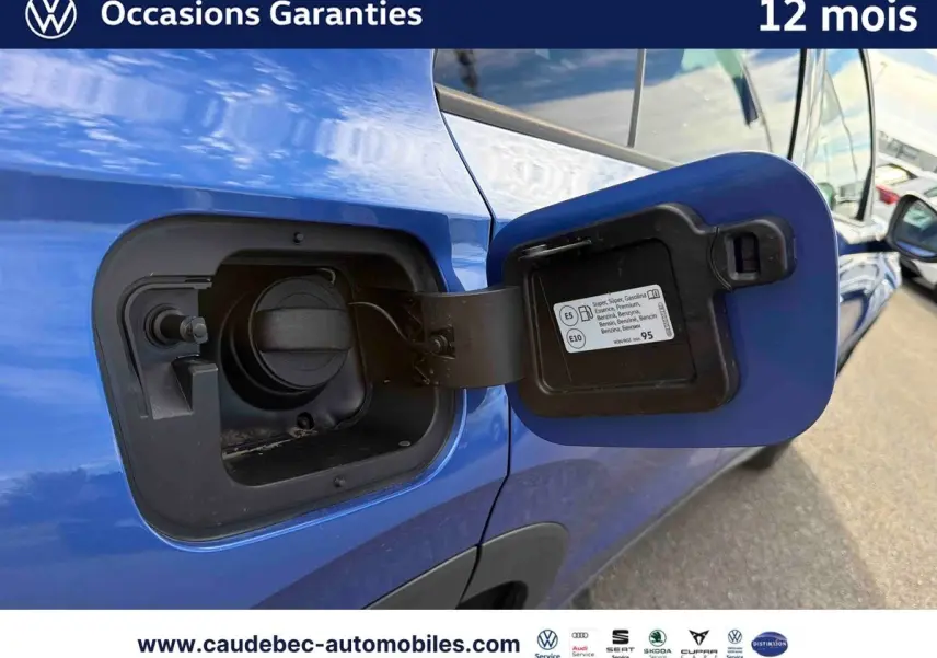 Gros plan sur la trappe à carburant ouverte côté gauche d’un Volkswagen T-Roc bleu métallisé stationné.