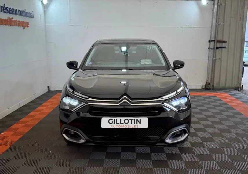 Citroën C4 PureTech 130 noir vue de face en intérieur, phares LED allumés et calandre distinctive.