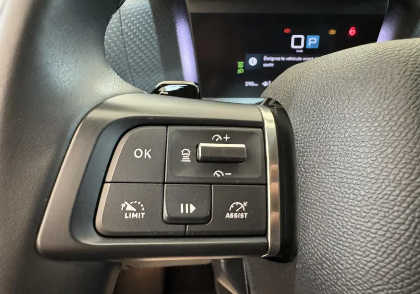 Gros plan sur les commandes au volant cuir noir de la Citroën C4 PureTech 130 EAT8 Shine 2023, avec affichage digital en arrière-plan.