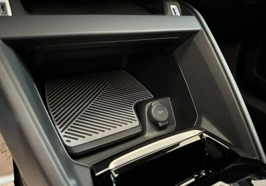 Détail de la console centrale noire d'une Citroën C4 PureTech 130 EAT8 Shine avec prise 12V et surface antidérapante.