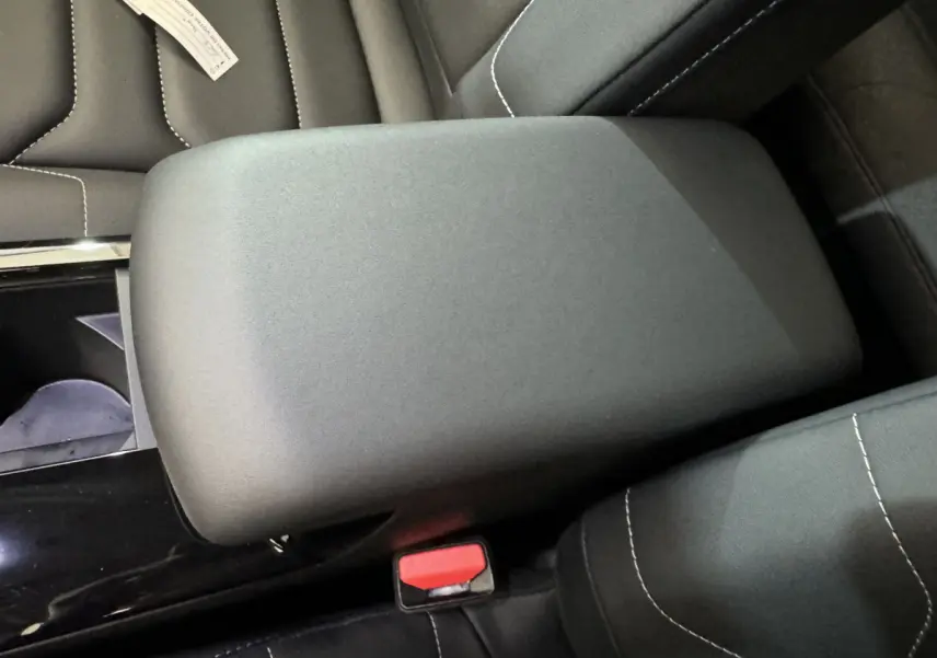 Gros plan sur l'accoudoir central noir et les sièges en tissu avec surpiqûres blanches d'une Citroën C4 PureTech 130 Shine 2023.