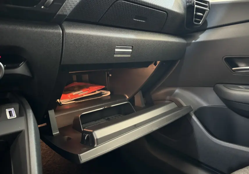 Vue intérieure côté passager du coffre à gants ouvert d'une Citroën C4 PureTech 130 EAT8 Shine noire, montrant des documents rouges.