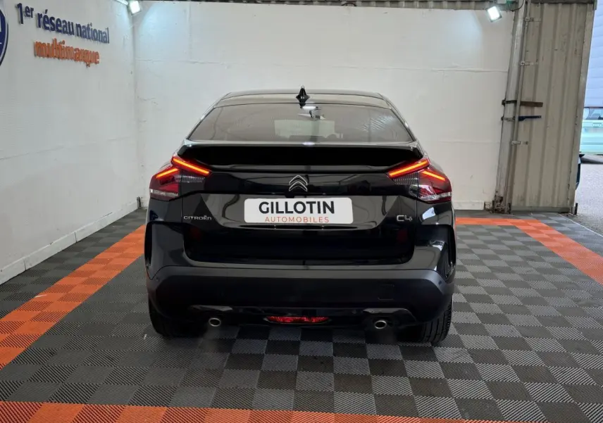 Vue arrière d'une Citroën C4 noire 2023 avec feux LED allumés dans un garage au sol damier noir et orange.