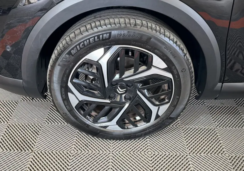 Gros plan sur la roue avant droite noire d'une Citroën C4 2023 avec jante alliage au design géométrique bicolore.