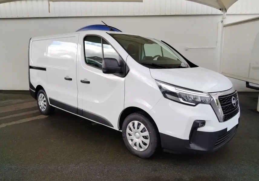 Vue 3/4 avant droit d'un utilitaire Nissan Primastar blanc avec calandre noire et jantes tôles sous abri.