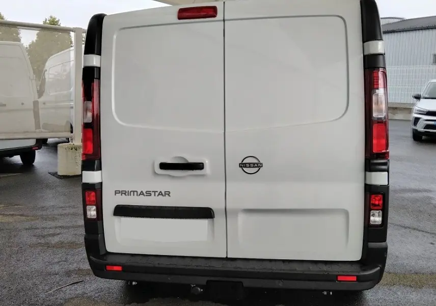 Vue arrière d'un utilitaire blanc Nissan Primastar 2025 avec porte battante et attelage visible.