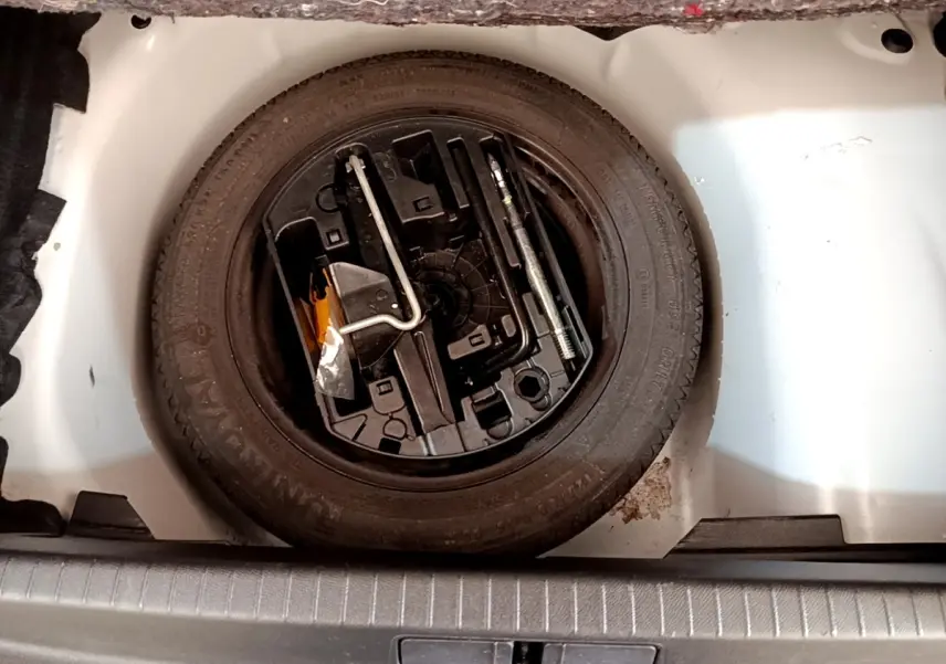 Vue plongeante sur la roue de secours noire et les outils dans le coffre blanc d'une Peugeot 208 blanche.